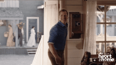 A Man In A Blue Shirt Is Standing In A Room With A Heart And Frame Logo GIF