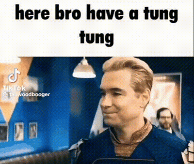 A Man In A Blue Shirt Is Standing In A Room With A Sign That Says `` Here Bro Have A Tung Tung '' . GIF