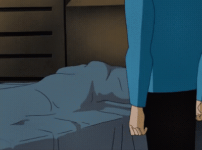 A Man In A Blue Shirt Is Standing In Front Of A Bed GIF