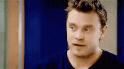 A Man In A Blue Shirt Is Standing In Front Of A Blue Door And Looking At The Camera . GIF
