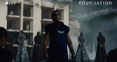 A Man In A Blue Shirt Is Standing In Front Of A Building With The Word Foundation Written On The Bottom GIF