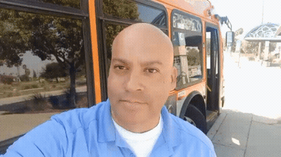 A Man In A Blue Shirt Is Standing In Front Of A Bus With The Number 8 On The Side GIF