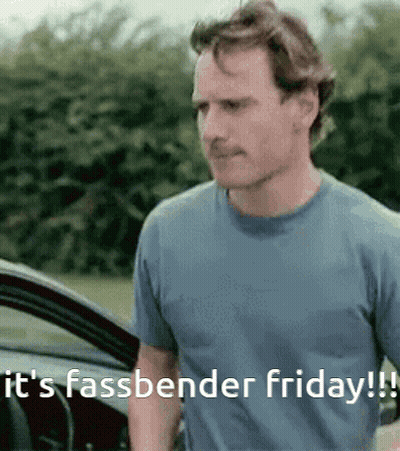 A Man In A Blue Shirt Is Standing In Front Of A Car And Says It 'S Fassbender Friday ! GIF