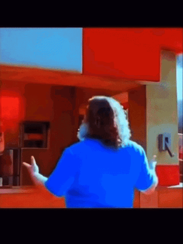 A Man In A Blue Shirt Is Standing In Front Of A Counter GIF