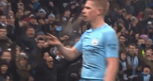 A Man In A Blue Shirt Is Standing In Front Of A Crowd Of People On A Soccer Field . GIF