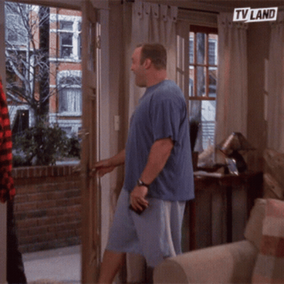 A Man In A Blue Shirt Is Standing In Front Of A Door With A Tv Land Sign Above Him GIF