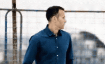 A Man In A Blue Shirt Is Standing In Front Of A Metal Fence . GIF