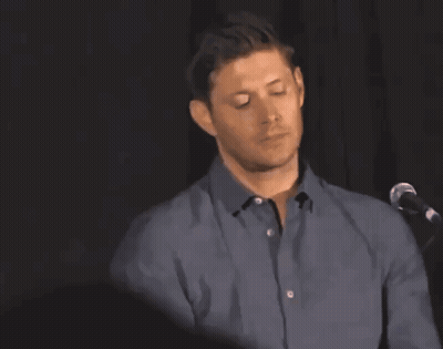 A Man In A Blue Shirt Is Standing In Front Of A Microphone With His Arm Raised GIF