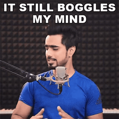 A Man In A Blue Shirt Is Standing In Front Of A Microphone With The Words `` It Still Boggles My Mind '' Above Him . GIF