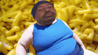 A Man In A Blue Shirt Is Standing In Front Of A Pile Of Macaroni And Cheese GIF