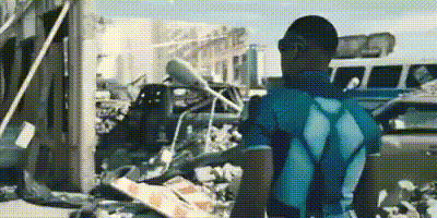 A Man In A Blue Shirt Is Standing In Front Of A Pile Of Rubble In A Parking Lot . GIF