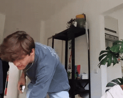 A Man In A Blue Shirt Is Standing In Front Of A Plant GIF