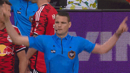A Man In A Blue Shirt Is Standing In Front Of A Purple Wall . GIF