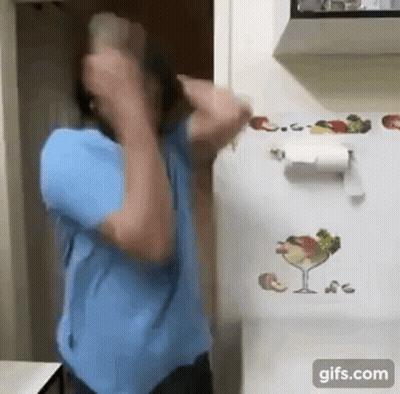 A Man In A Blue Shirt Is Standing In Front Of A Refrigerator With A Paper Towel Holder On It . GIF