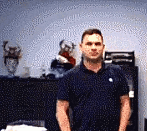 A Man In A Blue Shirt Is Standing In Front Of A Vase GIF