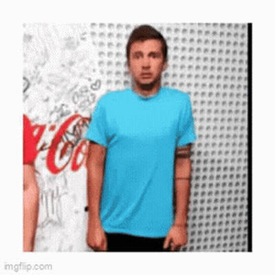 A Man In A Blue Shirt Is Standing In Front Of A Wall With A Coca Cola Logo On It GIF