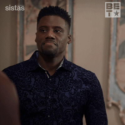 A Man In A Blue Shirt Is Standing In Front Of A Wall With A Sistas Logo On It GIF