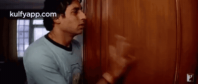 A Man In A Blue Shirt Is Standing In Front Of A Wooden Door In A Room . GIF