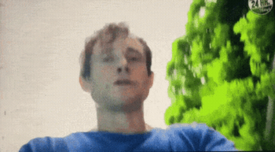 A Man In A Blue Shirt Is Standing In Front Of Trees And A 24 Hr Sign GIF