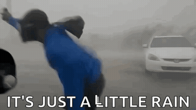 A Man In A Blue Shirt Is Standing In The Rain In Front Of A Car . GIF