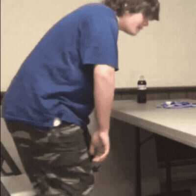 A Man In A Blue Shirt Is Standing Next To A Folding Table GIF