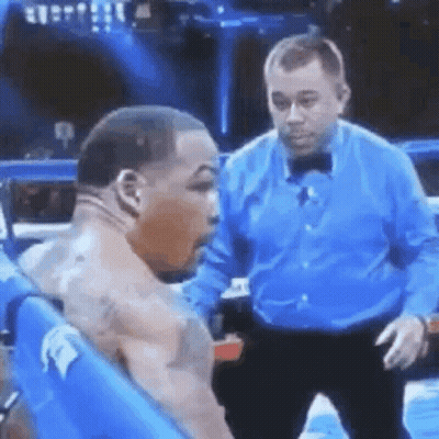 A Man In A Blue Shirt Is Standing Next To A Man In A Boxing Ring . GIF