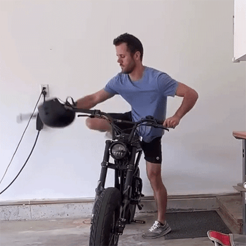 A Man In A Blue Shirt Is Standing Next To A Motorcycle Holding A Helmet GIF