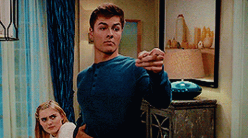 A Man In A Blue Shirt Is Standing Next To A Woman In A Living Room And Pointing At The Camera . GIF