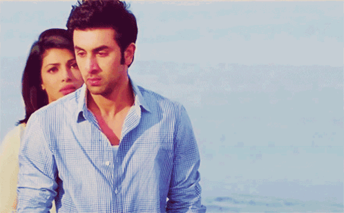 A Man In A Blue Shirt Is Standing Next To A Woman In A White Sweater GIF