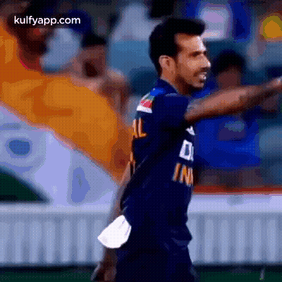 A Man In A Blue Shirt Is Standing On A Field And Pointing At Something . GIF