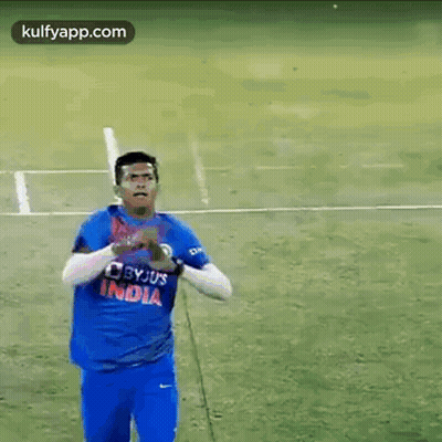 A Man In A Blue Shirt Is Standing On A Field Holding A Ball . GIF