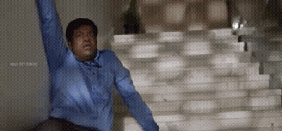 A Man In A Blue Shirt Is Standing On A Set Of Stairs With His Arms In The Air . GIF