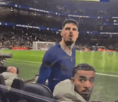 A Man In A Blue Shirt Is Standing On A Soccer Field While Another Man Looks On . GIF