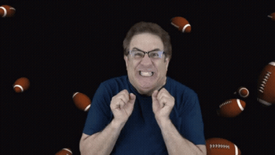 A Man In A Blue Shirt Is Surrounded By Footballs Flying Around Him GIF