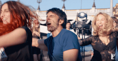 A Man In A Blue Shirt Is Surrounded By Women Dancing GIF