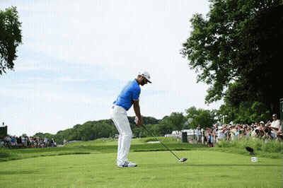 A Man In A Blue Shirt Is Swinging A Golf Club On A Green GIF