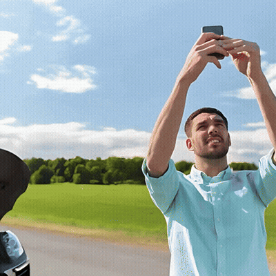 A Man In A Blue Shirt Is Taking A Picture Of A Field With His Phone GIF