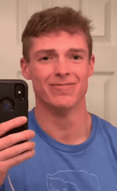 A Man In A Blue Shirt Is Taking A Selfie In Front Of A Mirror GIF