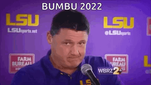 A Man In A Blue Shirt Is Talking Into A Microphone In Front Of A Purple Background . GIF
