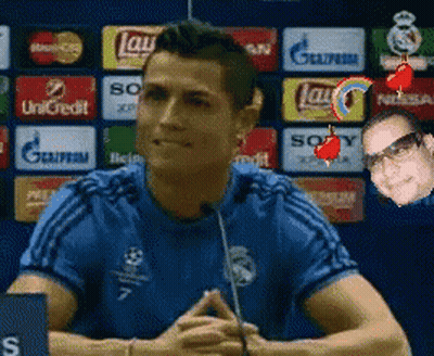 A Man In A Blue Shirt Is Talking Into A Microphone In Front Of A Wall With Advertisements For Lays And Sony GIF