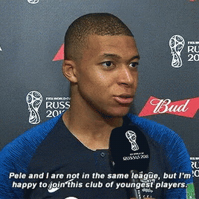 A Man In A Blue Shirt Is Talking Into A Microphone With A Bud Logo In The Background GIF