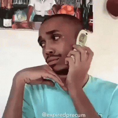 A Man In A Blue Shirt Is Talking On A Cell Phone With A Picture Of A Woman On The Wall Behind Him . GIF