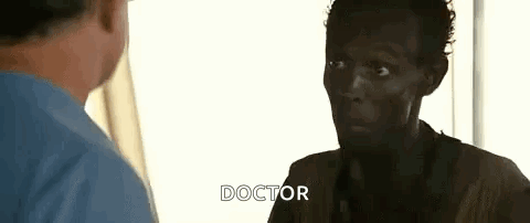 A Man In A Blue Shirt Is Talking To A Doctor In A Room . GIF