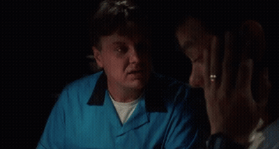 A Man In A Blue Shirt Is Talking To Another Man In A Dark Room . GIF