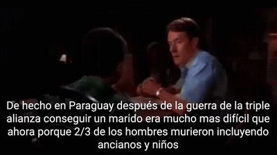 A Man In A Blue Shirt Is Talking To Another Man In A Dark Room In Spanish GIF