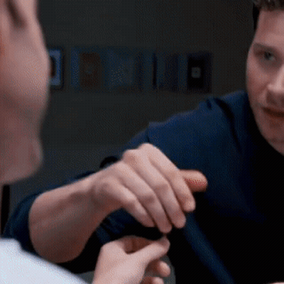 A Man In A Blue Shirt Is Talking To Another Man In A Dark Room GIF