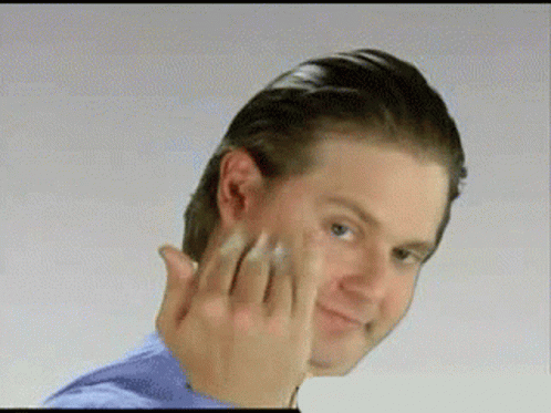 A Man In A Blue Shirt Is Touching His Face GIF