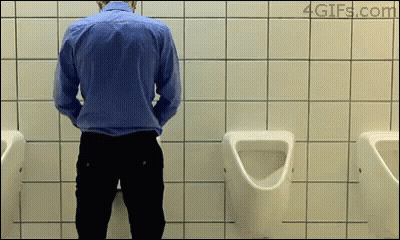 A Man In A Blue Shirt Is Urinating In A Bathroom GIF