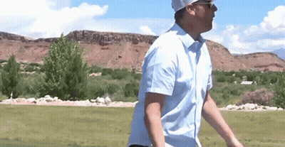 A Man In A Blue Shirt Is Walking On A Golf Course . GIF