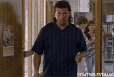 A Man In A Blue Shirt Is Walking Out Of A Doorway . GIF